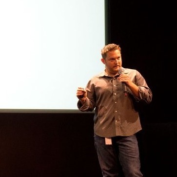 Darren Haas holding a microphone while speaking on a stage.