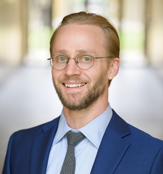 Roy Heidelberg headshot. He is in a blue suit standing in front of a window.