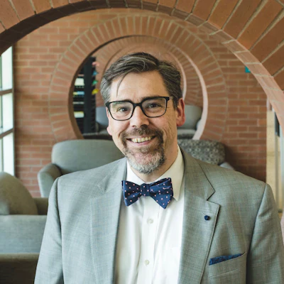 Tristan Denley headshot he is wearing a grey suit with a bowtie.