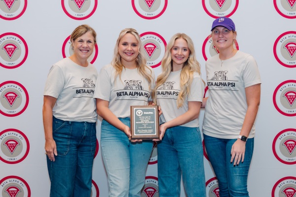 Four people in front of a large banner holding a plaque. 